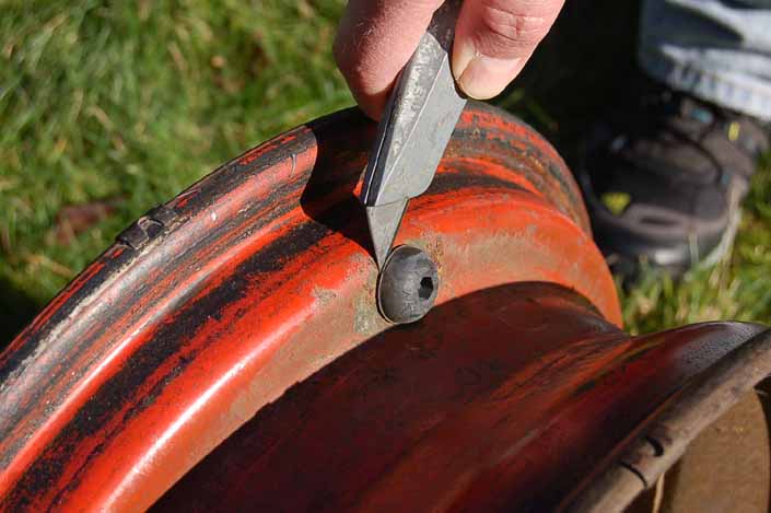 Photo shows a utility knife being used to cut-off the old valve stem from the back side of the vintage trailer wheel